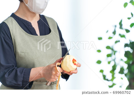 A woman wearing a mask and peeling an apple A woman wearing a mask and peeling an apple 69960702