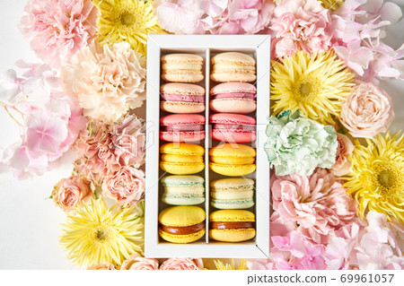 round beautiful sweets macaroni in a festive box with flowers on a flowers background. Still life with macaroni cakes and different flower. round beautiful sweets macaroni in a festive box with flowers on a flowers background. Still life with macaroni cakes and different flower. 69961057