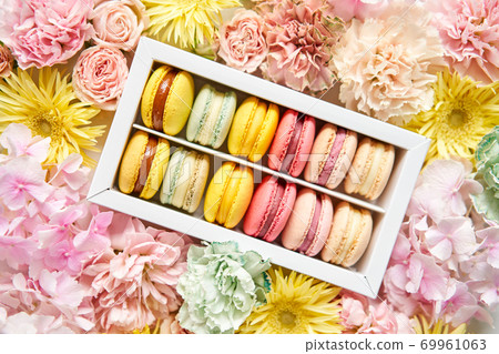 round beautiful sweets macaroni in a festive box with flowers on a flowers background. Still life with macaroni cakes and different flower. round beautiful sweets macaroni in a festive box with flowers on a flowers background. Still life with macaroni cakes and different flower. 69961063
