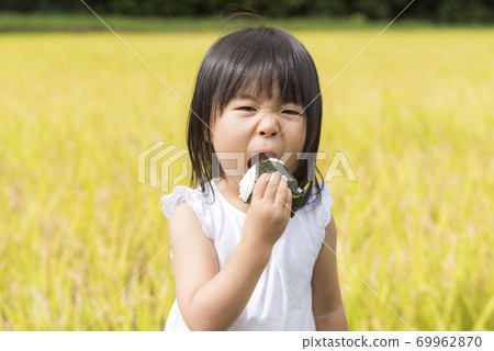 一個孩子在秋天的稻田裡用米耳吃美味的新米飯 一個孩子在秋天的稻田裡用米耳吃美味的新米飯 69962870