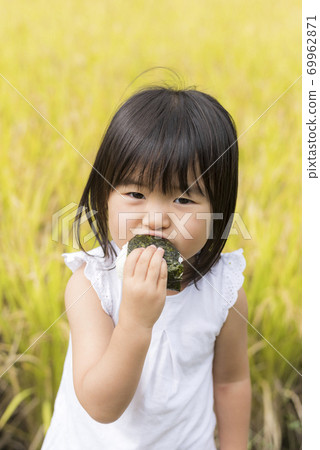一個孩子在秋天的稻田裡用米耳吃美味的新米飯 一個孩子在秋天的稻田裡用米耳吃美味的新米飯 69962871