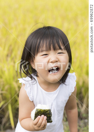 A child eating delicious new rice balls in an autumn rice field with rice ears A child eating delicious new rice balls in an autumn rice field with rice ears 69962872