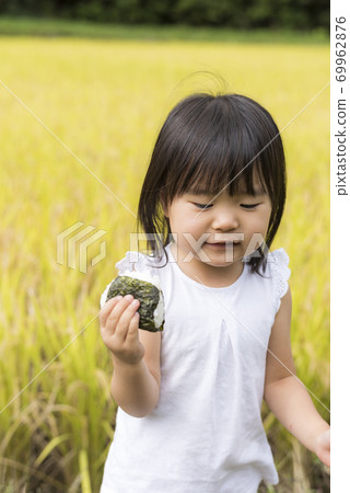 A child eating delicious new rice balls in an autumn rice field with rice ears A child eating delicious new rice balls in an autumn rice field with rice ears 69962876