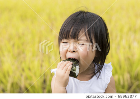 A child eating delicious new rice balls in an autumn rice field with rice ears A child eating delicious new rice balls in an autumn rice field with rice ears 69962877