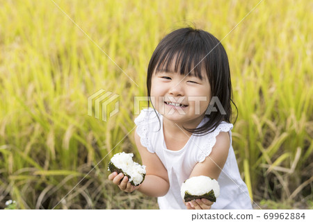 A child eating delicious new rice balls in an autumn rice field with rice ears A child eating delicious new rice balls in an autumn rice field with rice ears 69962884