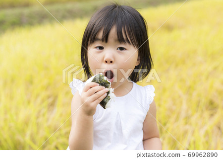 A child eating delicious new rice balls in an autumn rice field with rice ears A child eating delicious new rice balls in an autumn rice field with rice ears 69962890