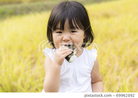 A child eating delicious new rice balls in an autumn rice field with rice ears A child eating delicious new rice balls in an autumn rice field with rice ears 69962892