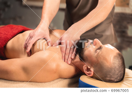 Physiotherapist giving Sports breast massage to bearded athlete in dark room of spa salon 69967005