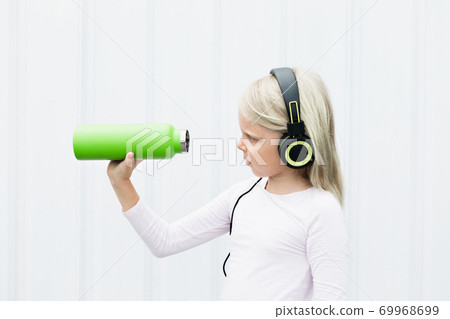 Young blond girl on white background drink fresh spring water from green reusable bottle 69968699