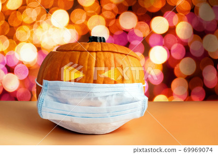 Pumpkin in a medical mask on the background of blurred lights. Pumpkin in a medical mask on the background of blurred lights. 69969074