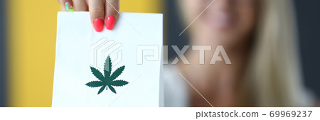 Female hand holds paper bag with an image of marijuana symbol closeup 69969237