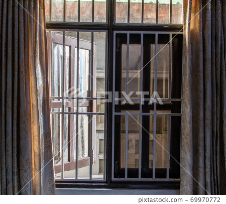A barred window open to the street, in close is wall of the next house. 69970772