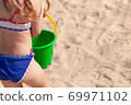 joyful three-year-old girl plays with a bucket and shoulder blade in the sand on the beach 69971102