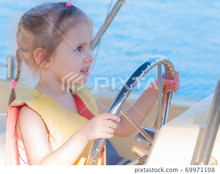 beautiful three-year-old girl at the helm of a boat on a clear day 69971108