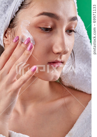 Girl's moisturizing her cheekbones with cream. 69971133
