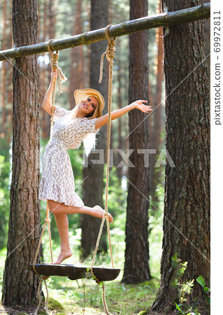 Blond woman with slender beautiful naked legs standing with on a rope swing Blond woman with slender beautiful naked legs standing with on a rope swing 69972811