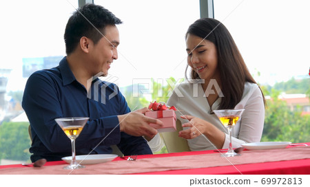 Romantic couple giving gift to lover at restaurant Romantic couple giving gift to lover at restaurant 69972813