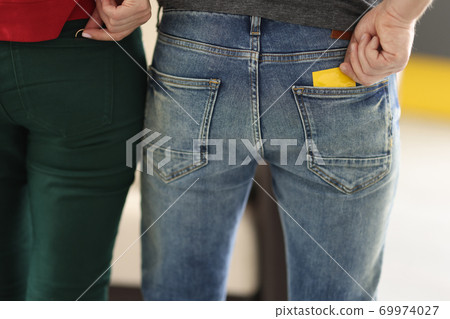 Two people stand with their backs, one takes out condom from pocket other wedding ring 69974027