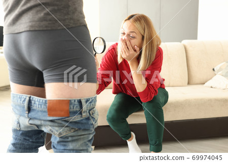 Man stands in shorts next to woman with magnifying glass, looking at her crotch in surprise. Man stands in shorts next to woman with magnifying glass, looking at her crotch in surprise. 69974045