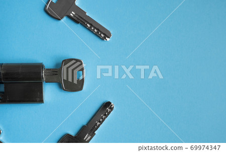 A door lock cylinder core with keys on the blue background. The cylinder of the lock with keys. Installing a new lock on the door. Spare parts for the door. 69974347