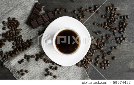 Coffee cup with cookies and chocolate with scattered coffee beans on linen and wooden table background. Mug of black coffee. Coffee cup with cookies and chocolate with scattered coffee beans on linen and wooden table background. Mug of black coffee. 69974432