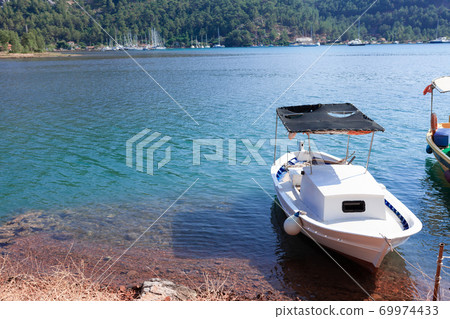 White small boat moored on the shore of the sea bay White small boat moored on the shore of the sea bay 69974433