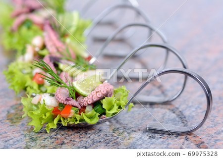 Seafood salad on party spoons served on a marble slab Seafood salad on party spoons served on a marble slab 69975328