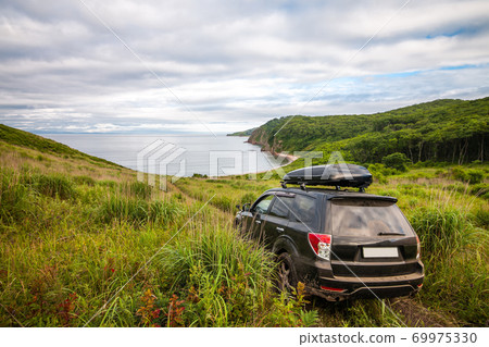 Black Subaru Forester with rooftop box on the road way down to the sea Black Subaru Forester with rooftop box on the road way down to the sea 69975330