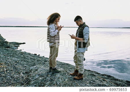 Couple using gadgets at lake Couple using gadgets at lake 69975653