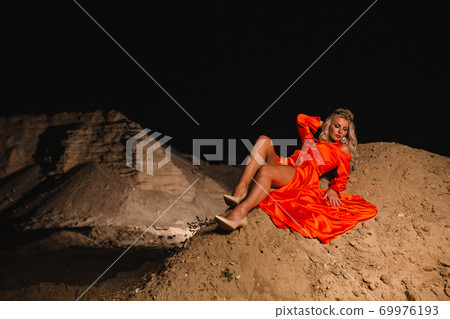 Blond woman in orange dress posing at the background of sand hill 69976193