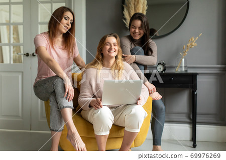 a group of girlfriends communicate with a friend via a video conference on a laptop. Friendship 69976269
