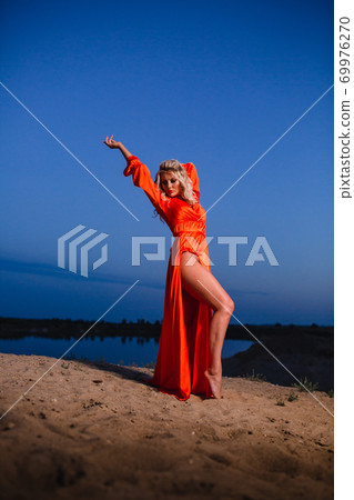 Young woman in bright orange dress posing at the background of blue sky 69976270