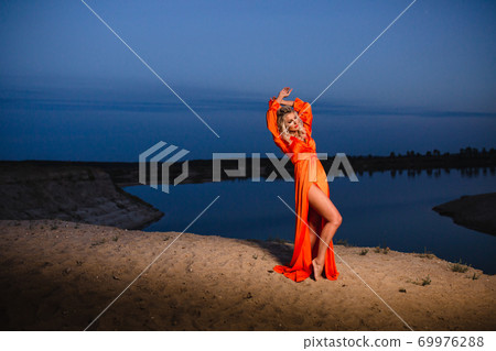 Young woman in bright orange dress posing at the background of blue sky 69976288