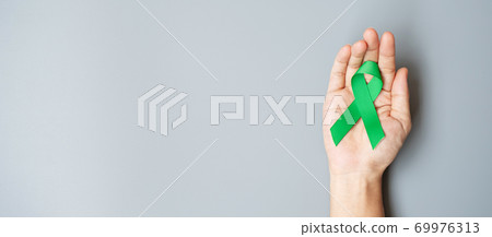 Man holding green Ribbon for supporting people living and illness. Liver, Gallbladders bile duct, kidney Cancer and Lymphoma Awareness month concept Man holding green Ribbon for supporting people living and illness. Liver, Gallbladders bile duct, kidney Cancer and Lymphoma Awareness month concept 69976313
