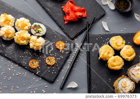 Set of sushi rolls, sauce, wasabi and hand with chopsticks on dark background. Top view. Flat lay. Japanese food Set of sushi rolls, sauce, wasabi and hand with chopsticks on dark background. Top view. Flat lay. Japanese food 69976373