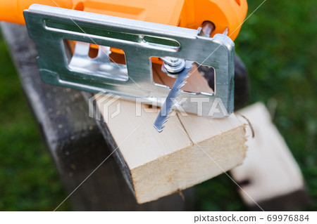 The concept of working with lumber. Electric jigsaw and wood board and sawdust. The concept of working with lumber. Electric jigsaw and wood board and sawdust. 69976884