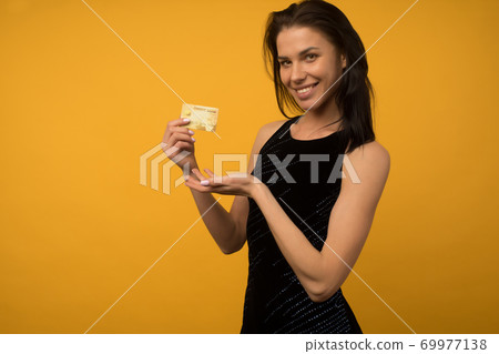 Photo of pleased young woman posing isolated over yellow wall background holding debit card. Photo of pleased young woman posing isolated over yellow wall background holding debit card. 69977138