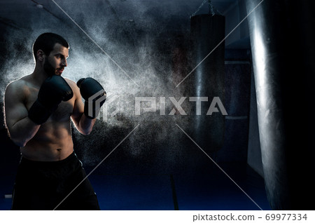 Thai boxing fighter on a dark background hits a boxing bag. Advertising Martial Arts Fitness Center 69977334