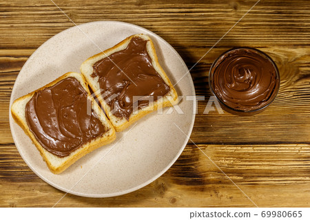 Two slices of bread with delicious chocolate hazelnut spread on wooden table. Top view Two slices of bread with delicious chocolate hazelnut spread on wooden table. Top view 69980665