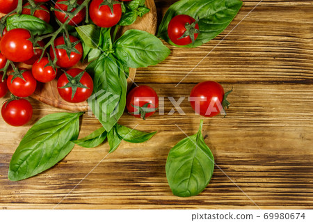 Fresh cherry tomatoes with green basil leaves on a wooden table. Top view 69980674