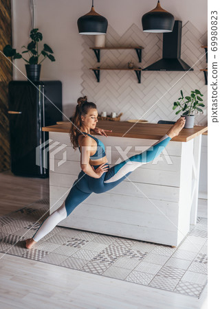 Fit woman doing front split standing with one foot on the floor and the other placed on the table. Fit woman doing front split standing with one foot on the floor and the other placed on the table. 69980823