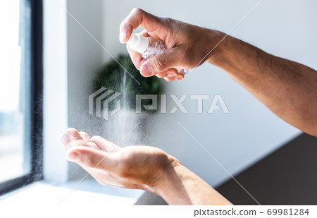 Young men use 70% alcohol spray to spray hands to get rid of bacteria and COVID-19 or CORONA viruses that destroy the respiratory system, COVID-19 virus protection concept. Young men use 70% alcohol spray to spray hands to get rid of bacteria and COVID-19 or CORONA viruses that destroy the respiratory system, COVID-19 virus protection concept. 69981284