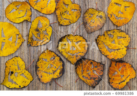 dry foliage on a wooden background. on the leaves made a scary mask. holiday of Halloween, leaf Jack lantern mask.  69981386