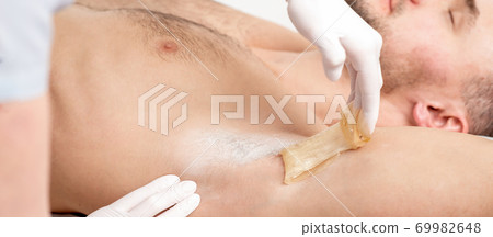 Cosmetologist applying wax paste on male armpit Cosmetologist applying wax paste on male armpit 69982648