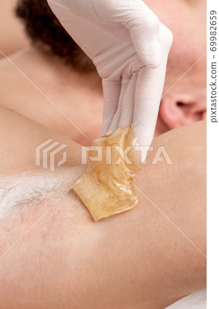 Cosmetologist applying wax paste on male armpit Cosmetologist applying wax paste on male armpit 69982659