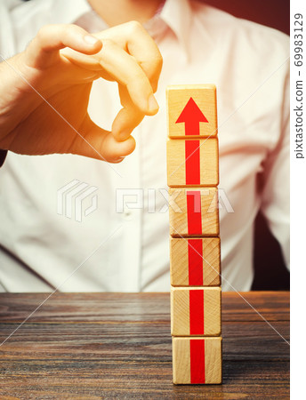 A man knocks down a tower of blocks with an arrow up. End of career, stop the progress and achievements. Eliminate the phenomenon, prevent further growth. Disruption business processes. Sabotage. 69983129