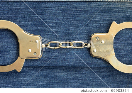 Police steel handcuffs lying on dark blue jeans background 69983824