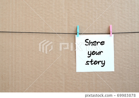 Share your story. Note is written on a white sticker that hangs with a clothespin on a rope on a background of brown cardboard 69983878