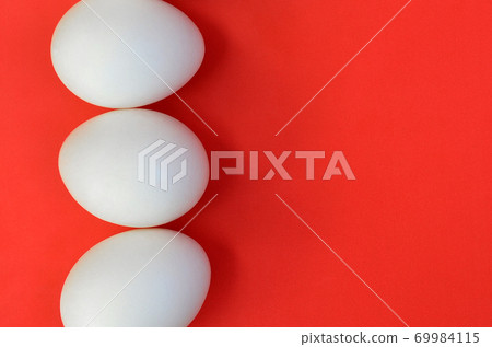 A few white eggs on a bright red background A few white eggs on a bright red background 69984115