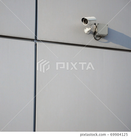 White surveillance camera built into the metal wall of the office building White surveillance camera built into the metal wall of the office building 69984125